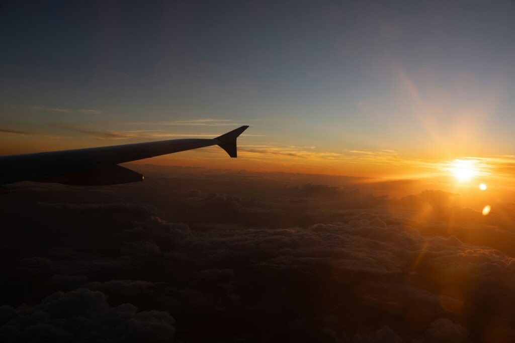 Airplane wing above golden sunset clouds, representing long-haul travel and jet lag recovery